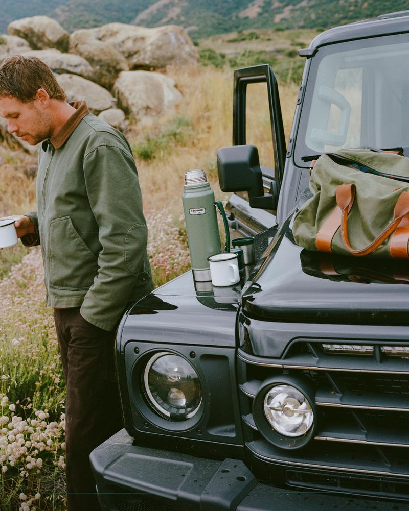 Two guests leaning against the front of a parked 4x4 in the hills, mugs in hand.