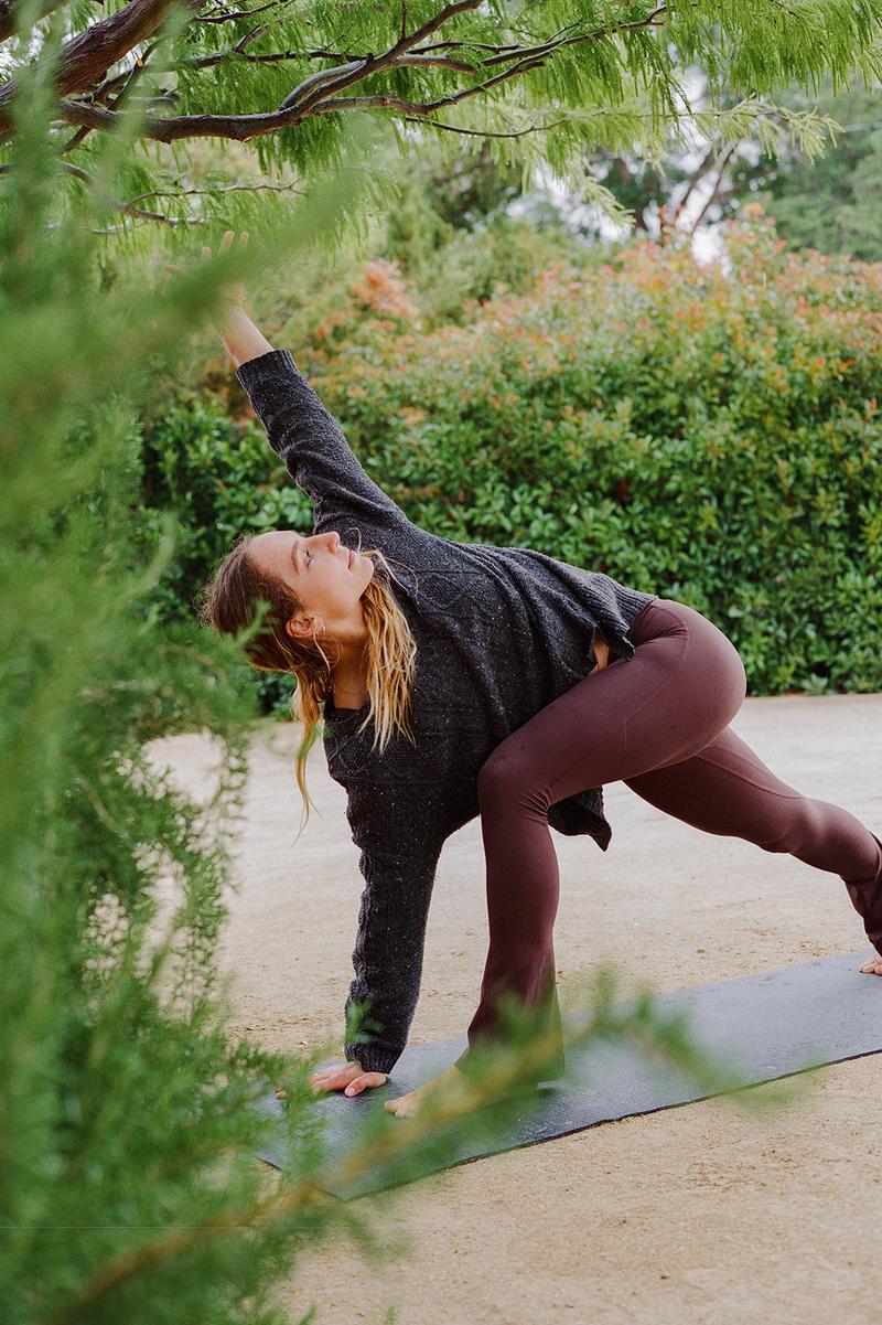 Woman stretching into a yoga pose outdoors among trees on a mat