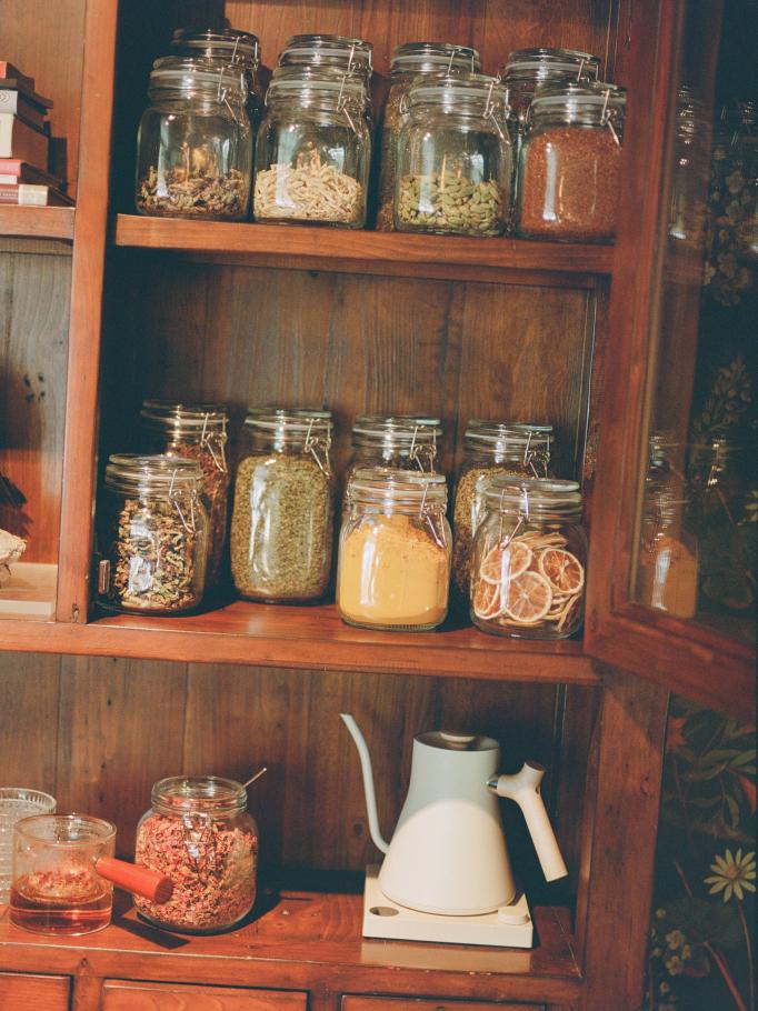Spices measured into a glass jar from a shelf of pantry jars
