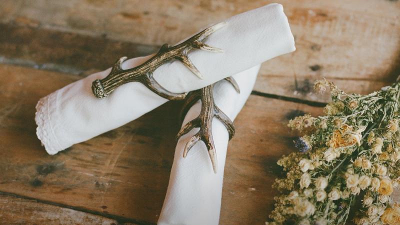 Antler napkin rings holding a folded white napkin beside dried wildflowers
