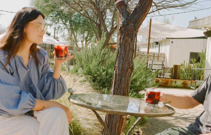 Two guests relaxing at a patio table in the shade with red cocktails in hand