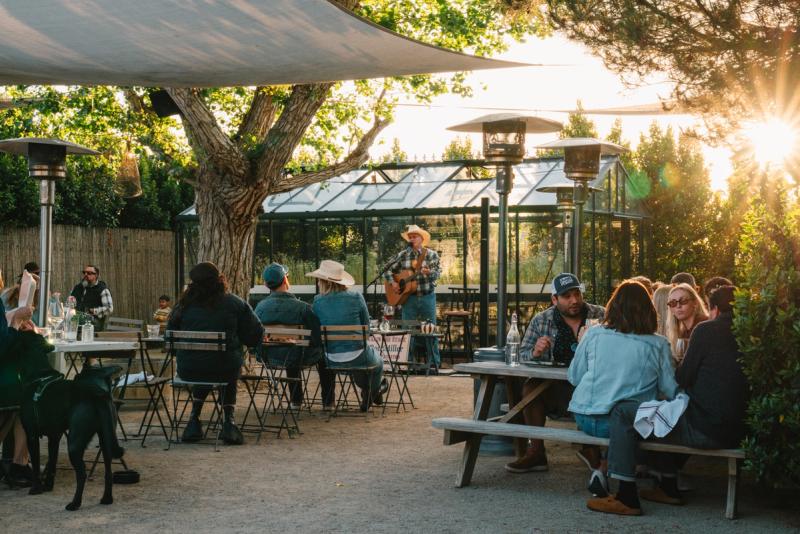 Guests gathered under a shade sail in the courtyard at golden hour with a musician playing