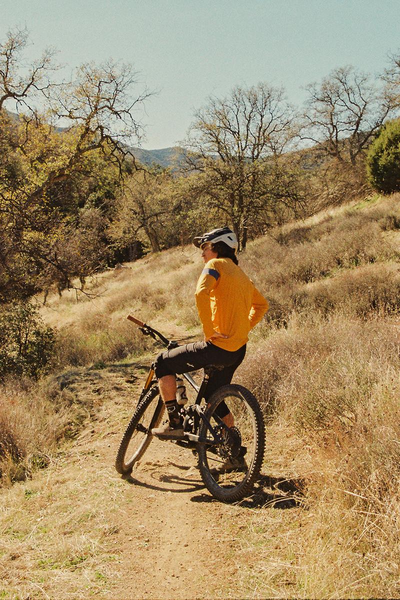 Mountain biker pausing on a dirt trail lined with oak trees and dry grass