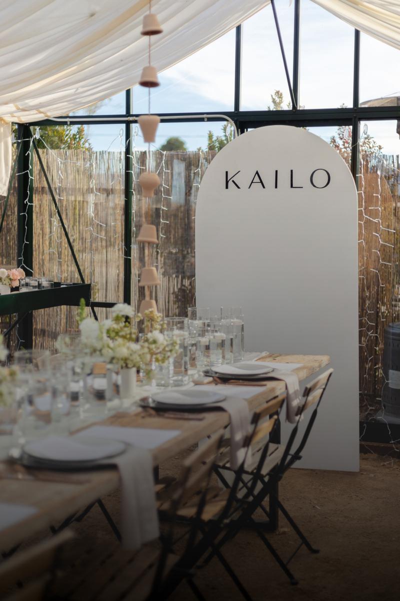 An outdoor reception table set beneath a Kailo sign and string lights