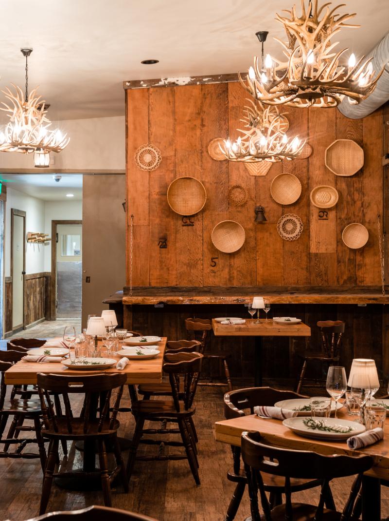 Antler chandeliers and woven baskets over a wood-paneled dining room