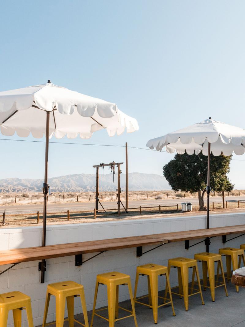 Scalloped white umbrellas over a yellow-stooled bar facing the desert