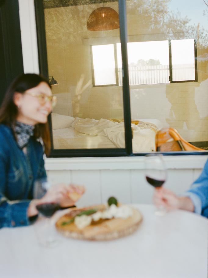 Guests toasting with wine over a cheese board seen through a window