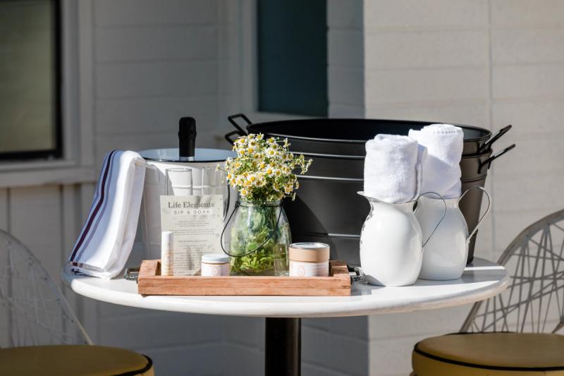 A bistro table set with a tray of bath products, towels and a jar of wildflowers.