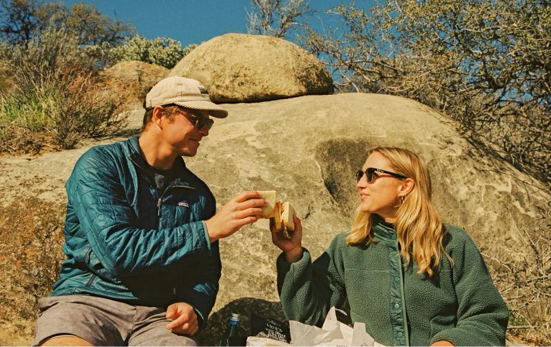 A couple cheersing their sandwiches mid-hike