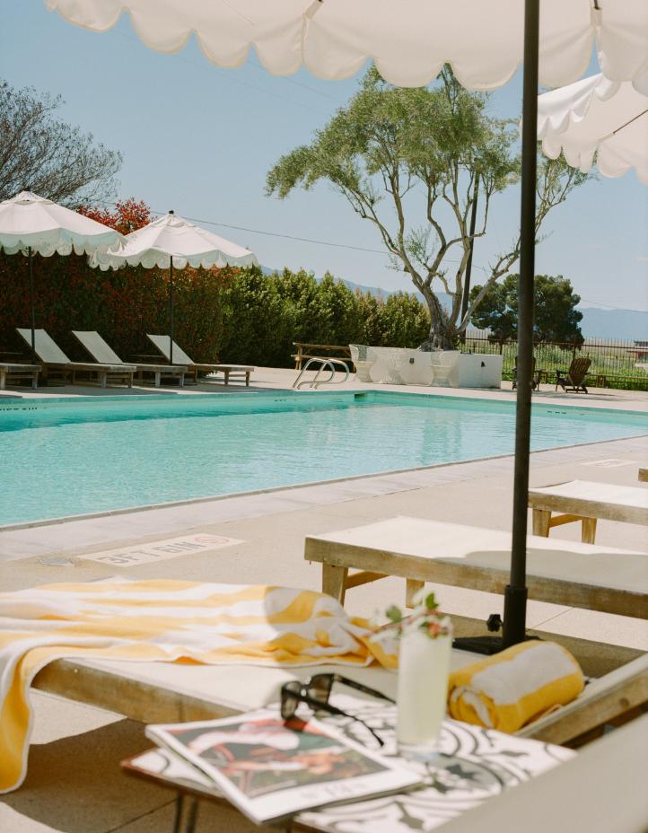 The pool at Cuyama Buckhorn, with scalloped umbrellas, loungers, and a striped towel and drink in the foreground.