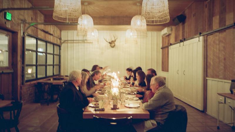 Diners gathered at a long candlelit table beneath a mounted set of antlers
