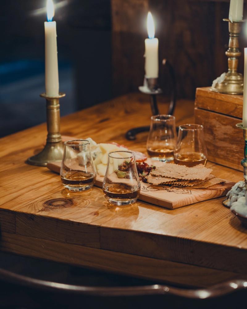 Lit candles and pours of whiskey set out for a tasting on a wood table
