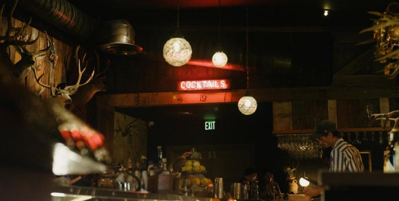 A glowing red Cocktails sign lights the wood-paneled bar at night