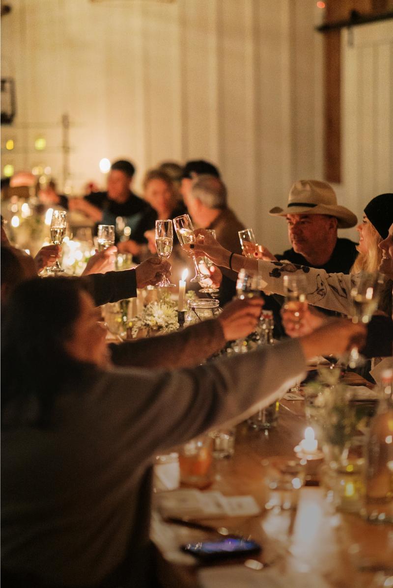 Guests raising champagne glasses in a toast at a candlelit long table