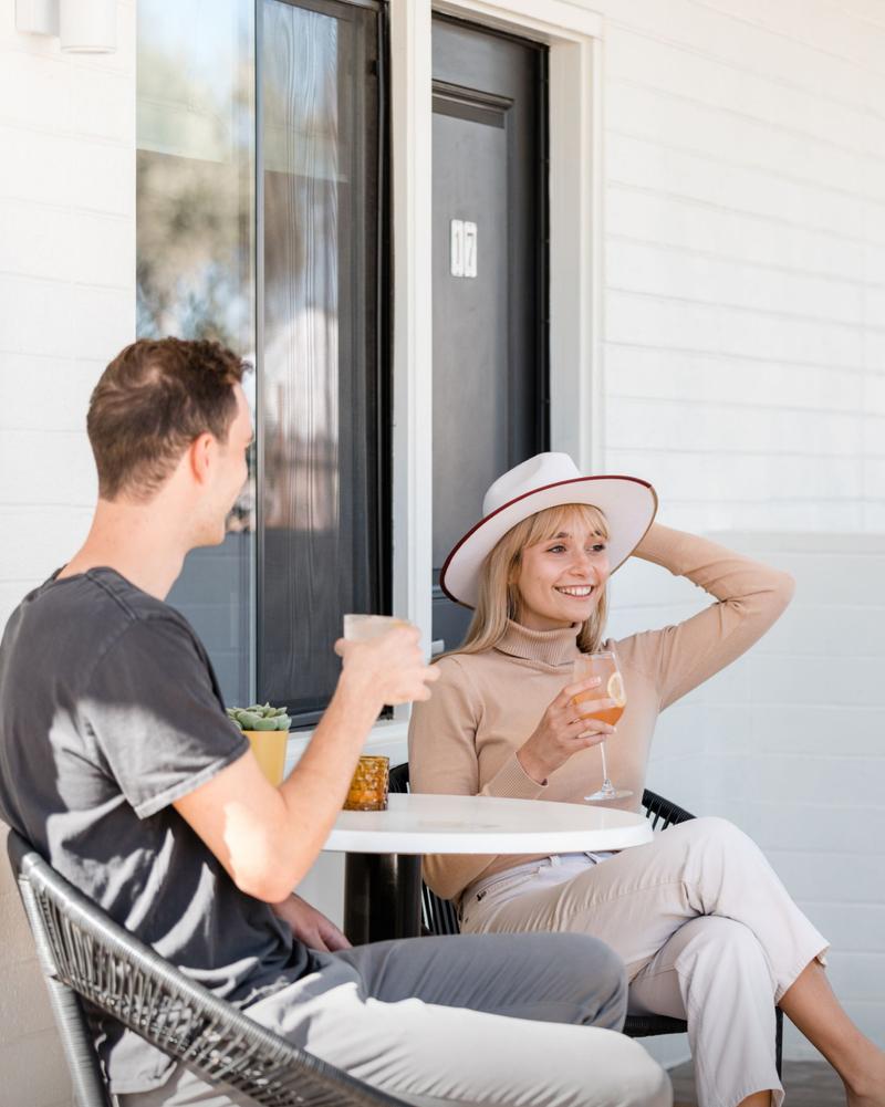 A couple relax with drinks at a bistro table outside their motel room door