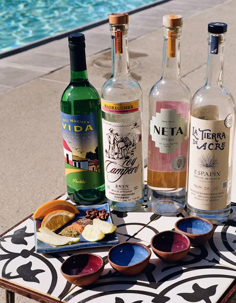 A selection of mezcal bottles sitting on a pool side table with the pool in the background.