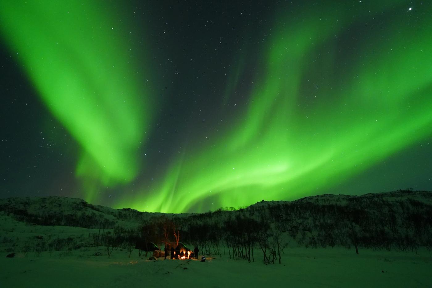 A cozy campfire under crazy glowing Northern Lights