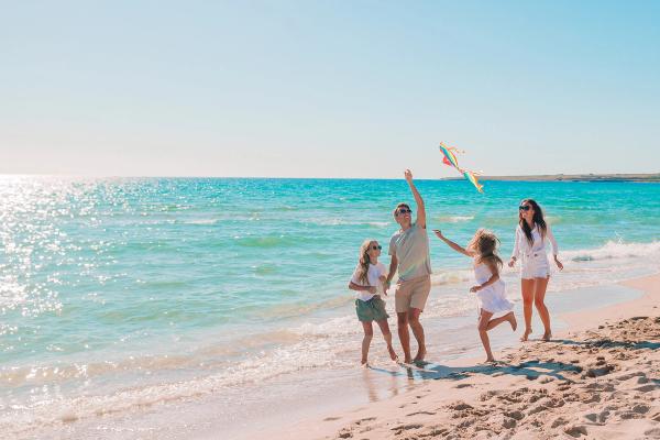 A family flying a kite on a calm, shallow beach in Lombok, Indonesia
