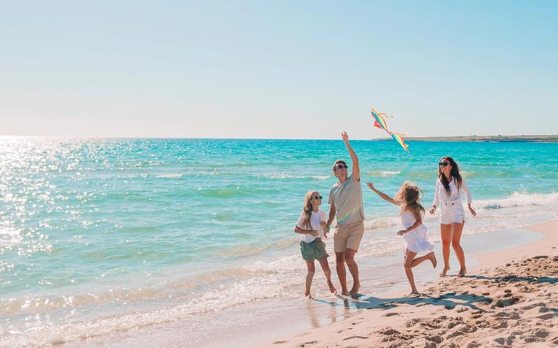 A family flying a kite on a calm, shallow beach in Lombok, Indonesia