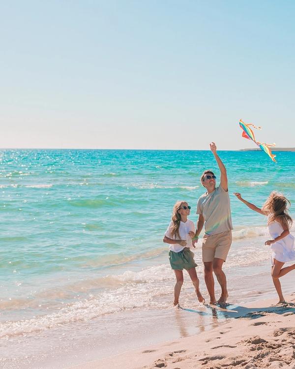 A family flying a kite on a calm, shallow beach in Lombok, Indonesia