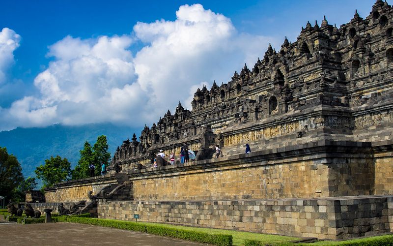 Visitors walking the stone terraces of Borobudur temple under a blue sky in Central Java