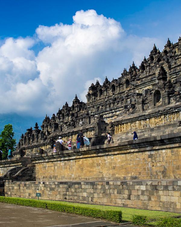 Visitors walking the stone terraces of Borobudur temple under a blue sky in Central Java