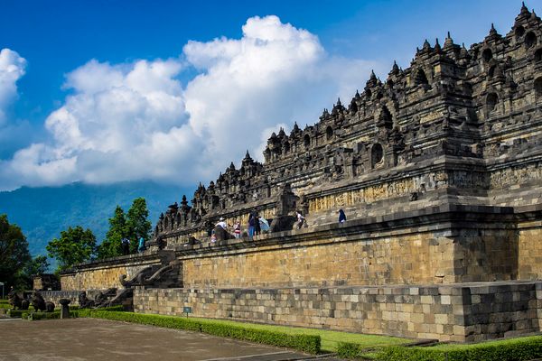 Visitors walking the stone terraces of Borobudur temple under a blue sky in Central Java