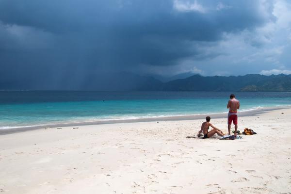 Empty white-sand beach on Gili Meno with turquoise shallows and the mountains of Lombok across the strait
