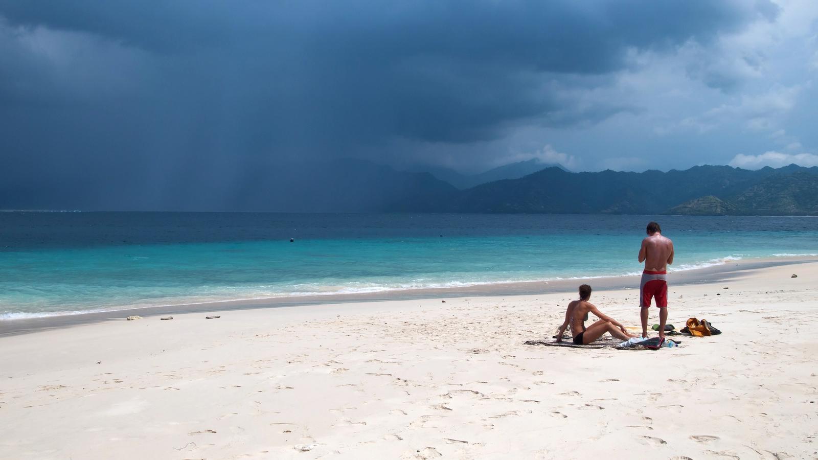 Empty white-sand beach on Gili Meno with turquoise shallows and the mountains of Lombok across the strait