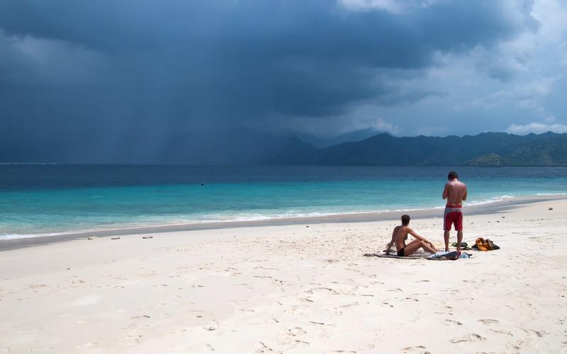 Empty white-sand beach on Gili Meno with turquoise shallows and the mountains of Lombok across the strait