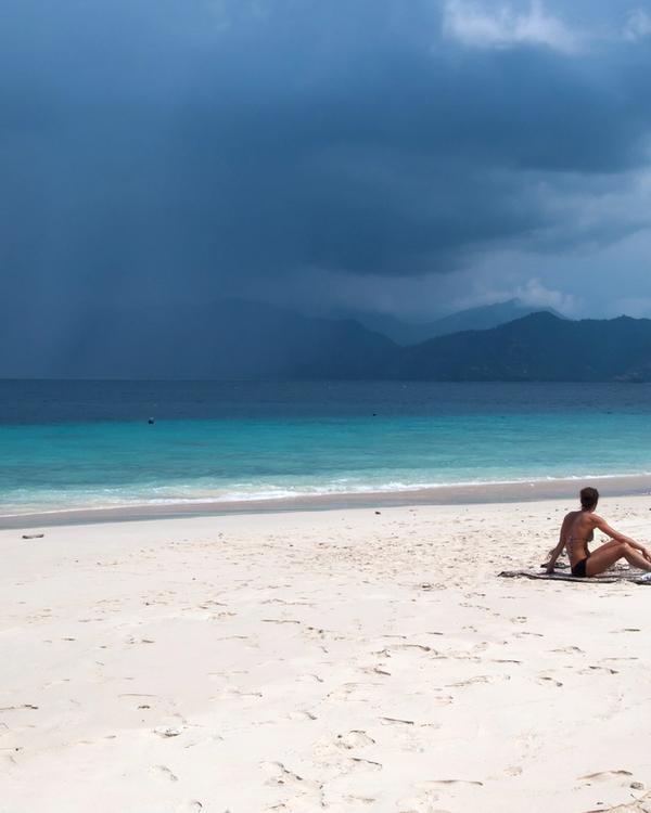 Empty white-sand beach on Gili Meno with turquoise shallows and the mountains of Lombok across the strait