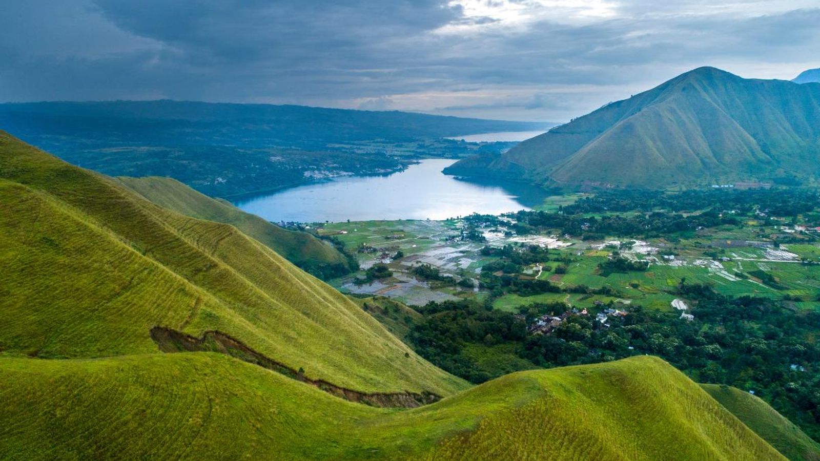 Lake Toba seen from the green hills above the shore, with Batak villages and rice fields below