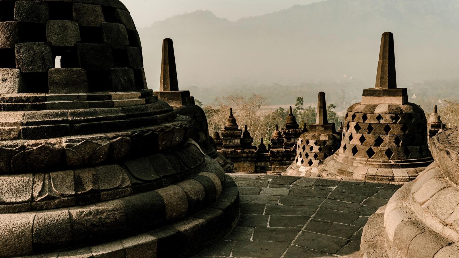 Stupas on the upper terrace of Borobudur at sunrise, with haze over the Magelang plain below