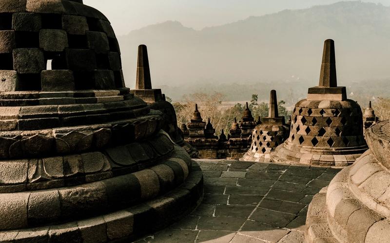 Stupas on the upper terrace of Borobudur at sunrise, with haze over the Magelang plain below