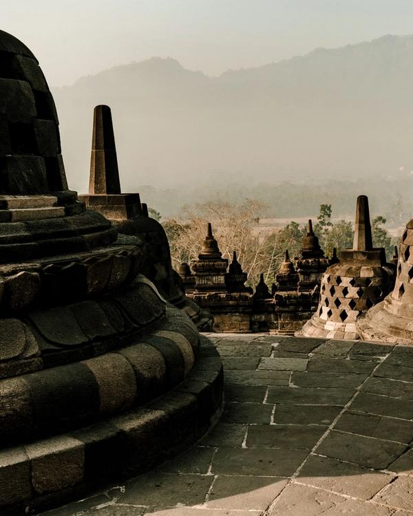 Stupas on the upper terrace of Borobudur at sunrise, with haze over the Magelang plain below