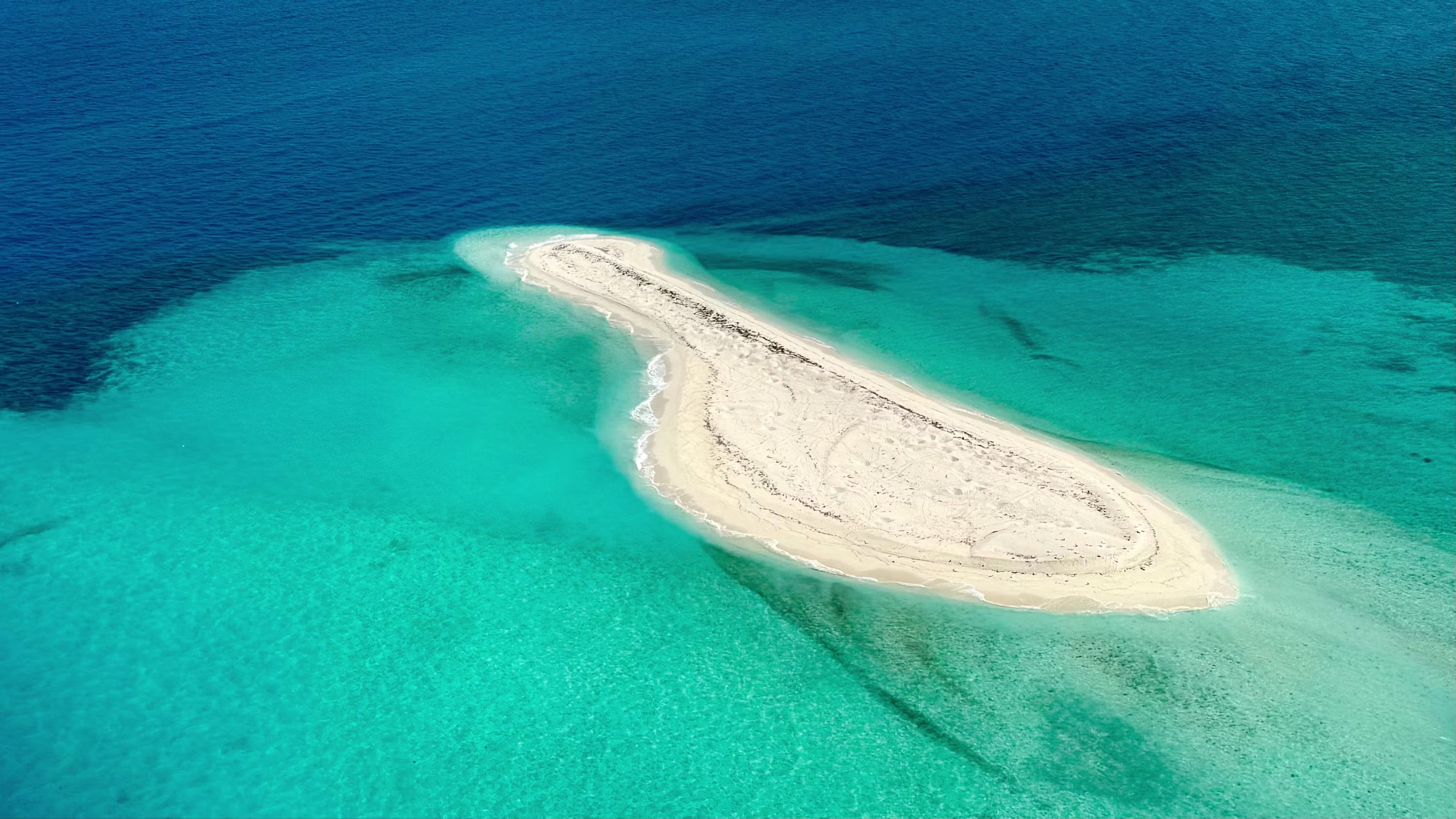 Aerial view of a bare sand bar ringed by shallow turquoise reef in the Java Sea