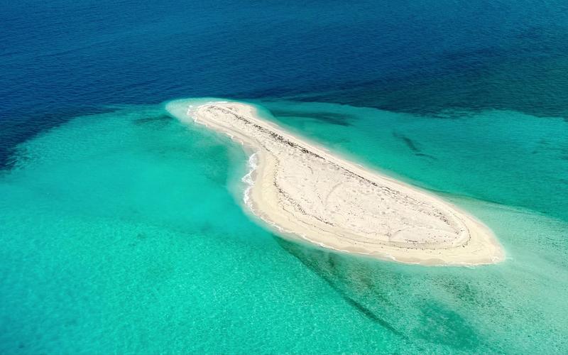 Aerial view of a bare sand bar ringed by shallow turquoise reef in the Java Sea