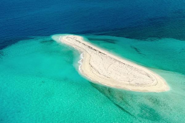 Aerial view of a bare sand bar ringed by shallow turquoise reef in the Java Sea