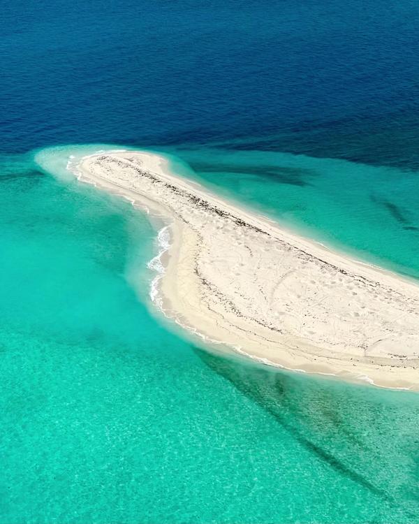 Aerial view of a bare sand bar ringed by shallow turquoise reef in the Java Sea