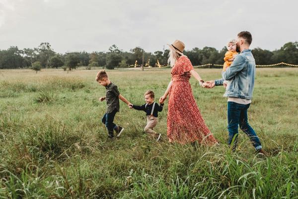 Parents and three young children walking hand in hand through a meadow at golden hour