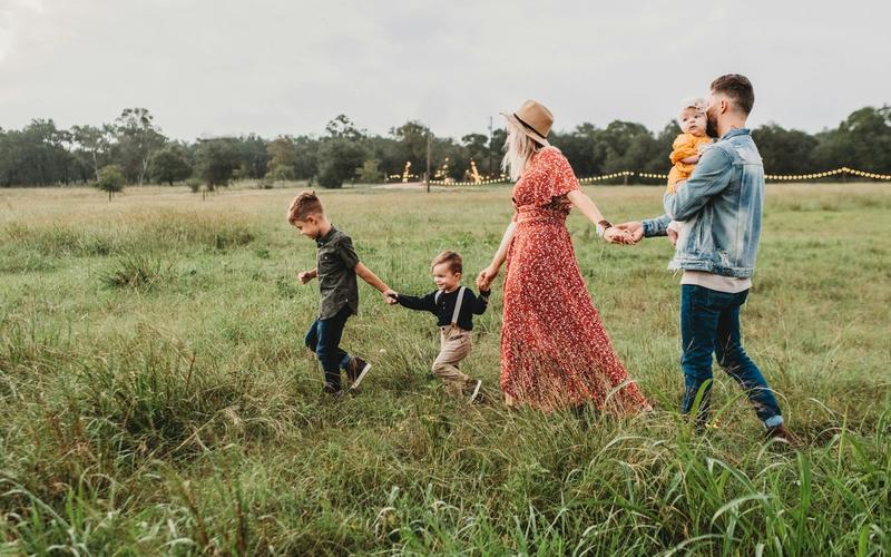 Parents and three young children walking hand in hand through a meadow at golden hour