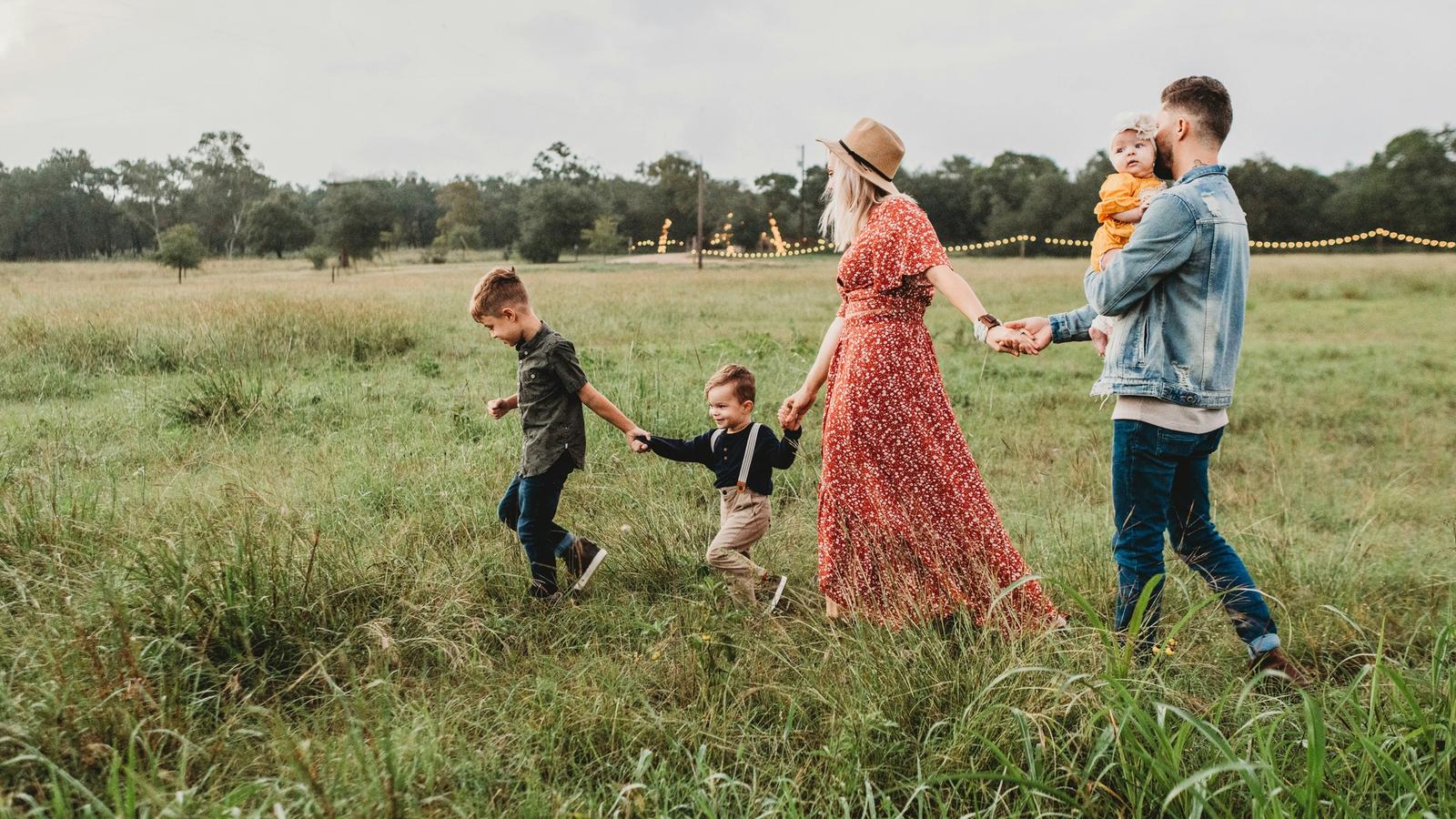 Parents and three young children walking hand in hand through a meadow at golden hour