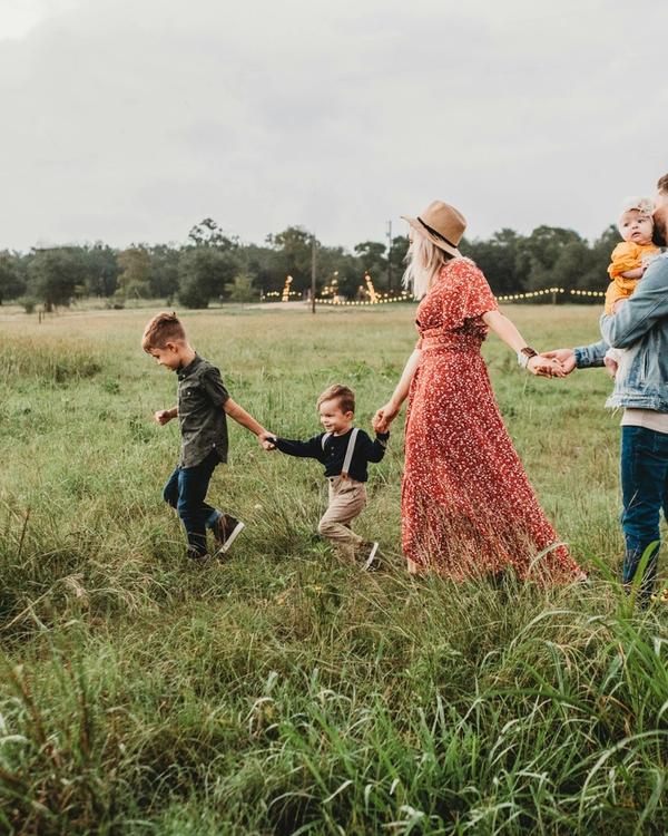 Parents and three young children walking hand in hand through a meadow at golden hour