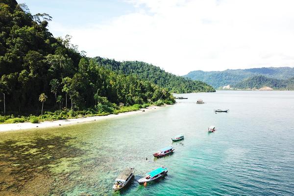 Wooden boats moored over shallow reef below a forested headland in Mandeh Bay, West Sumatra