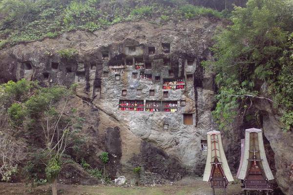 Lemo cliff burial site in Tana Toraja, Sulawesi, with carved rock niches, tau tau effigies and tongkonan-roofed grave structures