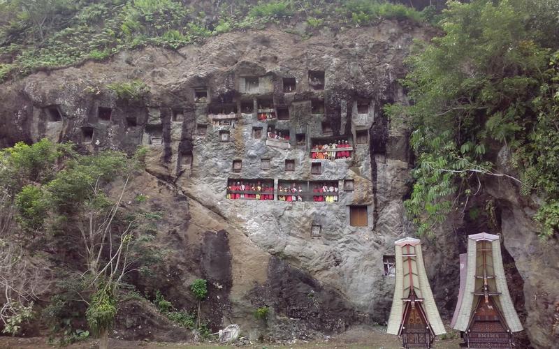 Lemo cliff burial site in Tana Toraja, Sulawesi, with carved rock niches, tau tau effigies and tongkonan-roofed grave structures