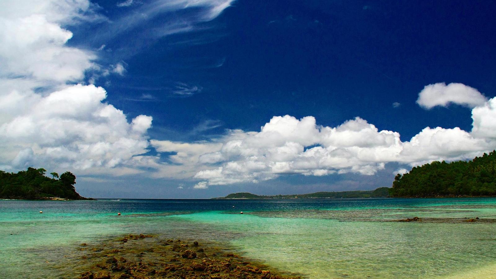 Shallow reef and turquoise water off Iboih beach on Pulau Weh, Aceh, with forested headlands under a bright sky