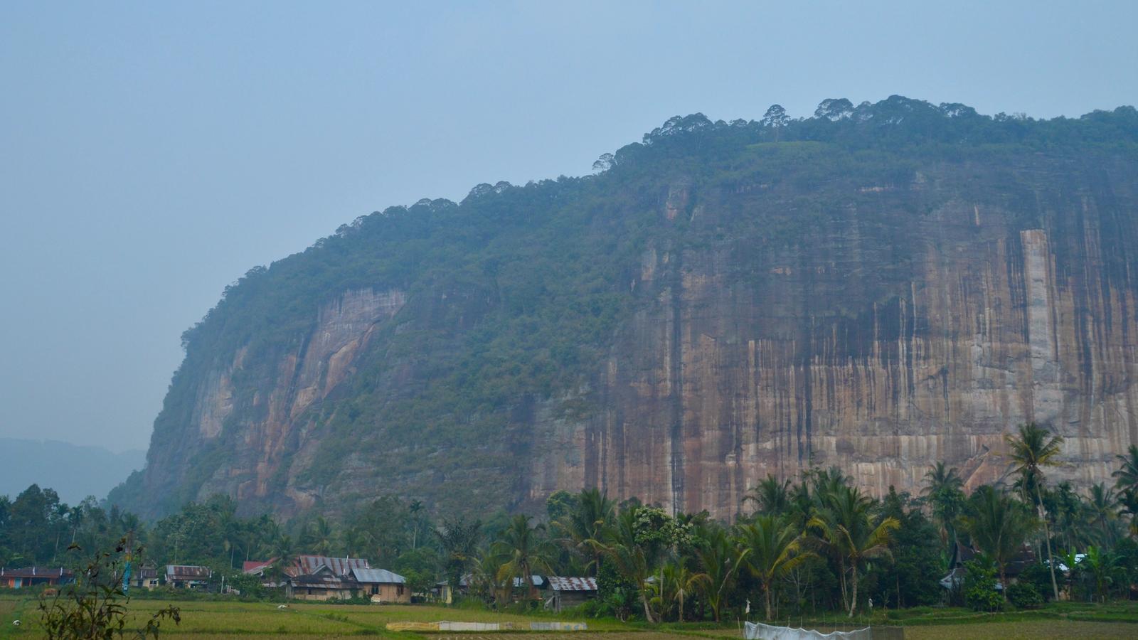 The sheer cliff walls of Harau Valley rising above rice fields and village houses in Lima Puluh Kota, West Sumatra