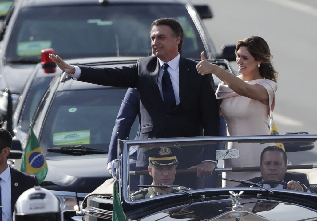 Flanked by first lady Michelle Bolsonaro, Brazil's President Jair Bolsonaro waves to the crowd as he rides in an open car after his swearing-in ceremony, in Brasilia, Brazil, Tuesday, Jan. 1, 2019. (AP Photo/Silvia Izquierdo)