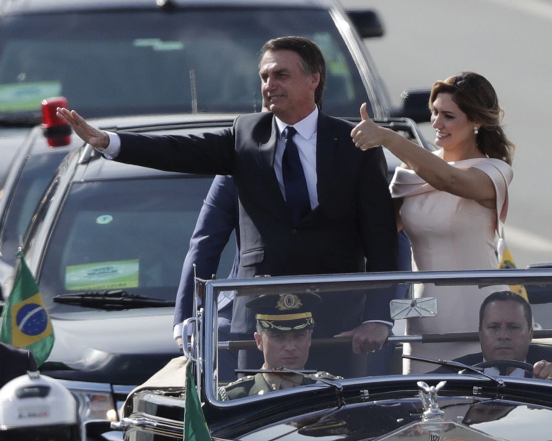 Flanked by first lady Michelle Bolsonaro, Brazil's President Jair Bolsonaro waves to the crowd as he rides in an open car after his swearing-in ceremony, in Brasilia, Brazil, Tuesday, Jan. 1, 2019. (AP Photo/Silvia Izquierdo)